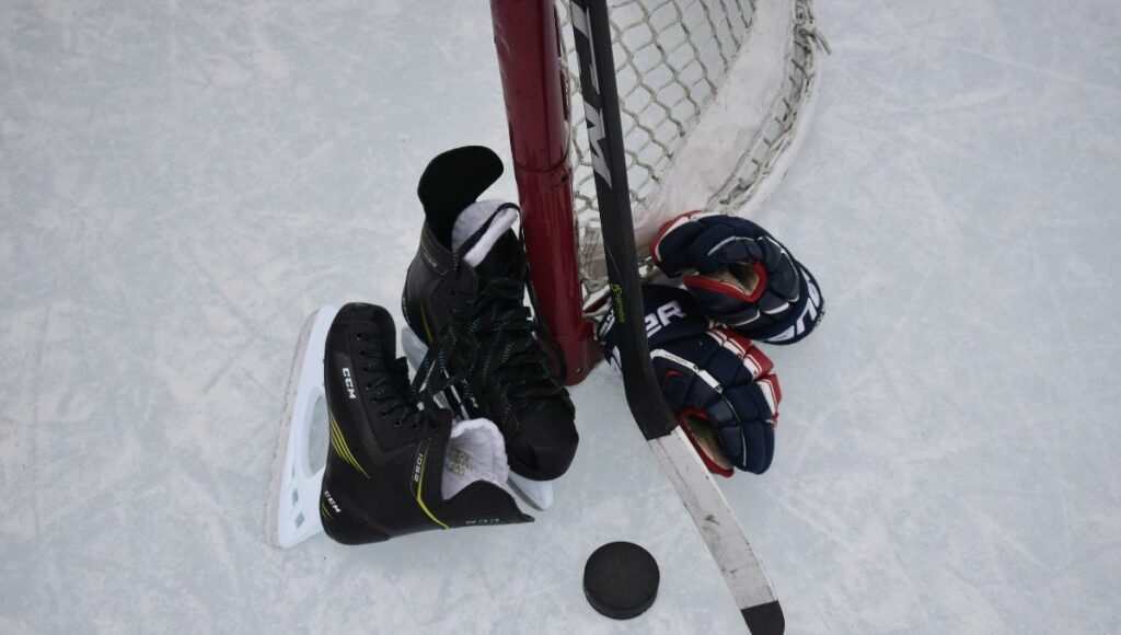 Ice hockey equipment including gloves, skates, puck and stick on the ice next to a goal